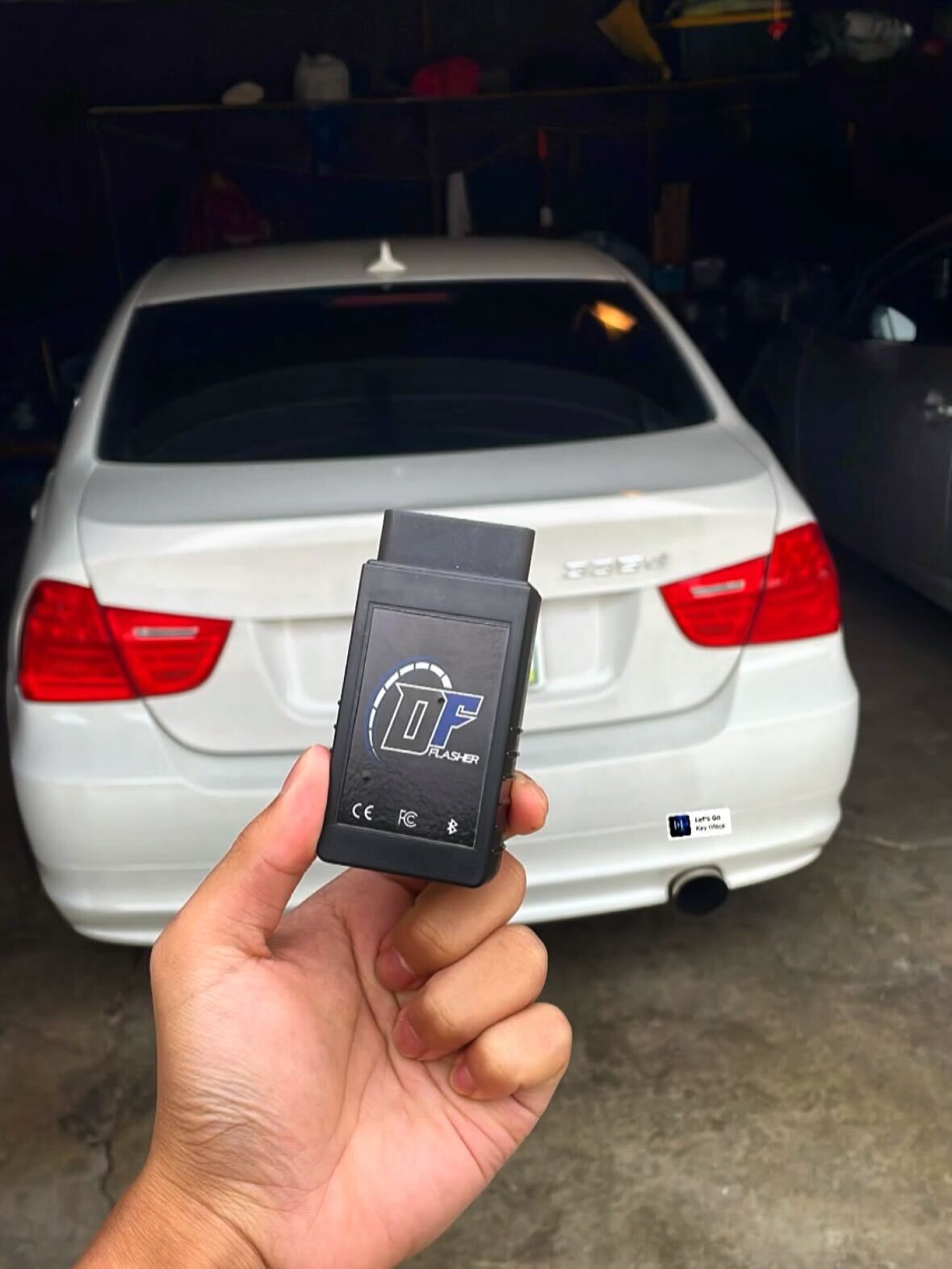 DFlasher OBD-II adapter held in front of white BMW 335d in garage