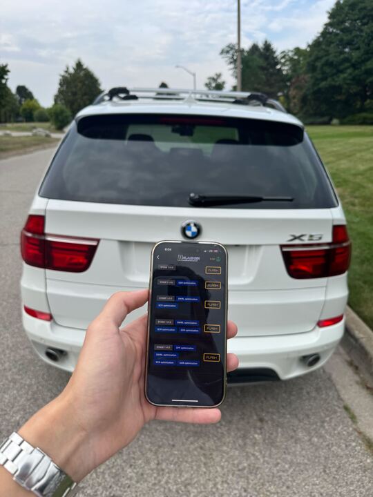 DFlasher adapter held near BMW X5 rear badge outdoors
